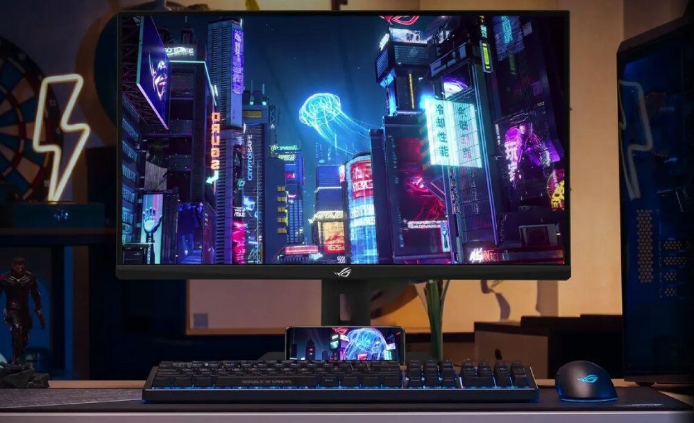 Monitor ASUS ROG Strix XG27UCG Monitor ustawiony na biurku z klawiaturą i telefonem umieszczonym w uchwycie w podstawie. Na ekranie futurystyczne miasto nocą, matryca, czas reakcji, rozmazanie, wyrazistość