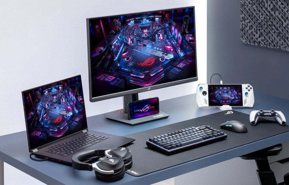Monitor ASUS ROG Strix XG27UCG Monitor na biurku wraz z laptopem, klawiaturą, myszką, słuchawkami, telefonem i konsolą przenośną. Na wszystkich ekranach wyświetlany ten sam motyw futurystycznej gry pinball, porty, podłączenie