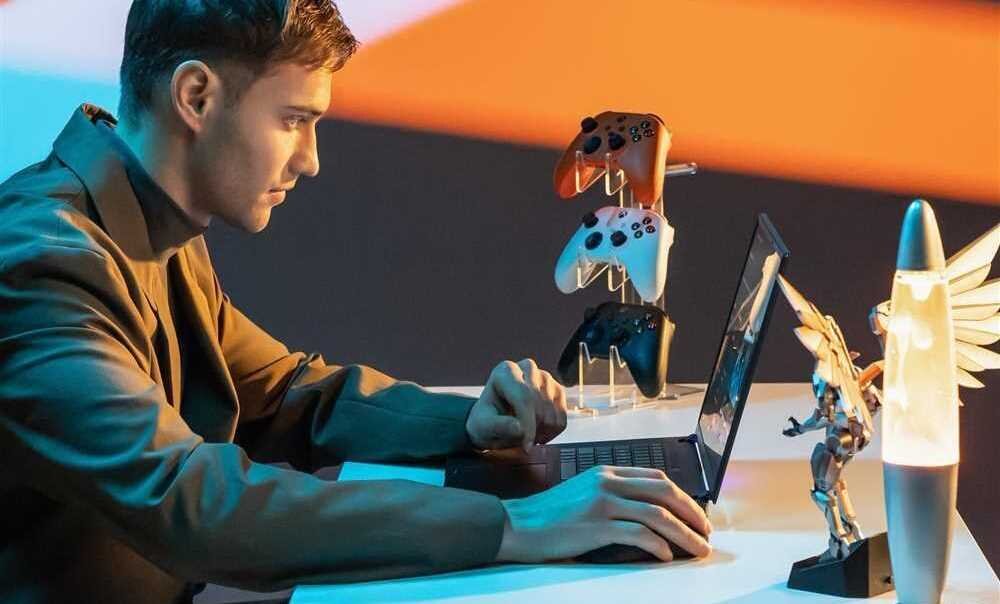 Mężczyzna siedzi przy biurku z laptopem GIGABYTE Aorus 16X i świecącą zabawką obok. - Intel Core HX WQXGA 165 Hz AI NVIDIA GeForce RTX