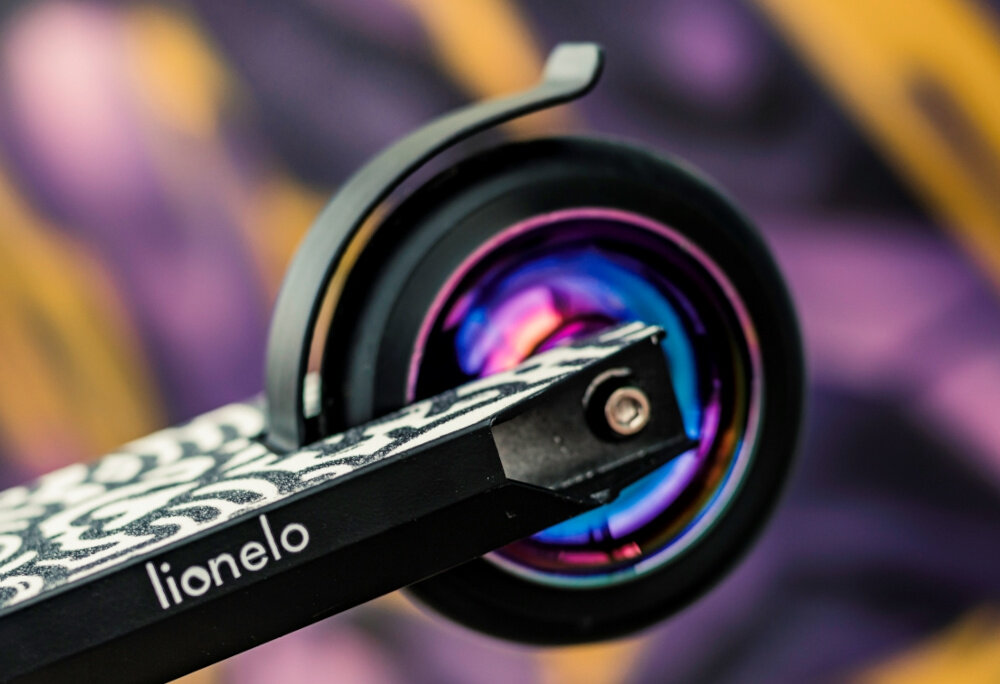 Hulajnoga wyczynowa LIONELO Whizz Wielokolorowy Czarno-fioletowy bezpieczenstwo tylny hamulec nozny bezpieczny system kompresji HIC sztywnosc wytrzymalosc polaczen