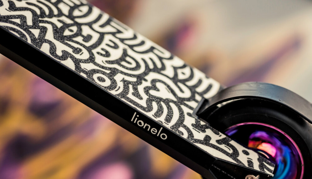 Hulajnoga wyczynowa LIONELO Whizz Wielokolorowy Czarno-fioletowy szeroki deck stabilna pozycja bezpieczna jazda anodyzowane aluminium wzmocnienie podestu duza odpornosc wytrzymalosc antyposlizgowa wykladzina