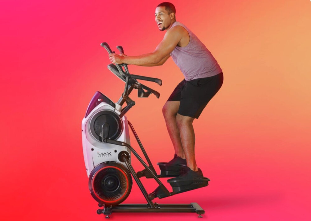 Orbitrek magnetyczno-powietrzny BOWFLEX M6i Max Trainer osoba ćwiczy na maszynie zdjęcie na kolorowym tle do domowych treningów wymiary 116 x 66 x 163 cm waga 67 kg solidne materiały przemyślana konstrukcja wbudowane uchwyty na bidon i tablet
