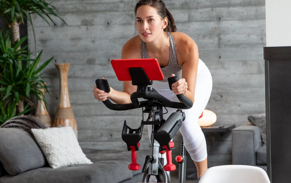 Rower spiningowy SCHWINN Indoor Cycling Schwinn 800IC osoba jedzie na rowerze bidon na uchwycie praktyczne dodatki uchwyt na media/urządzenia stacja ładowania USB-A uchwyt na bidon