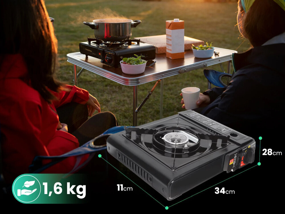 Kuchenka turystyczna EXTRALINK EX.39500 trawnik dwie osoby siedzą przy stoliku biwakowym na stoliku kuchenka i jedzenie na pierwszym planie kuchenka widoczna pod skosem podane wymiary i waga wymiary 34 × 28 × 11 cm łatwa do przenoszenia i przechowywania prosta obsługa dostosowanie płomienia do aktualnych potrzeb