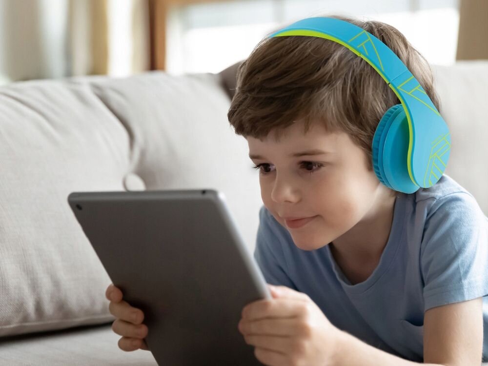 Słuchawki nauszne POWERLOCUS P2 Kids mikrofon nauka zdalna kompatybilność, dziecko z założonymi słuchawkami nausznymi trzymające tablet