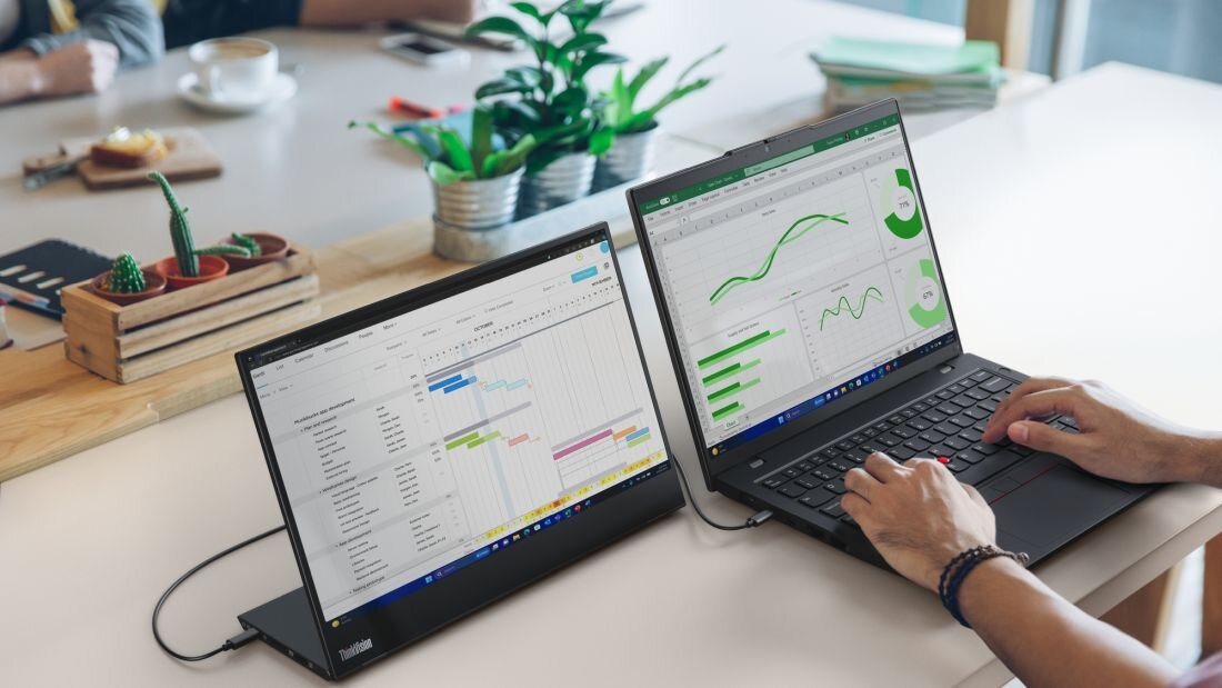 Mężczyzna pracujący na laptopie Lenovo ThinkPad z dodatkowym monitorem ThinkVision pokazującym wykresy analityczne. - materiały z recyklingu pokonsumenckiego