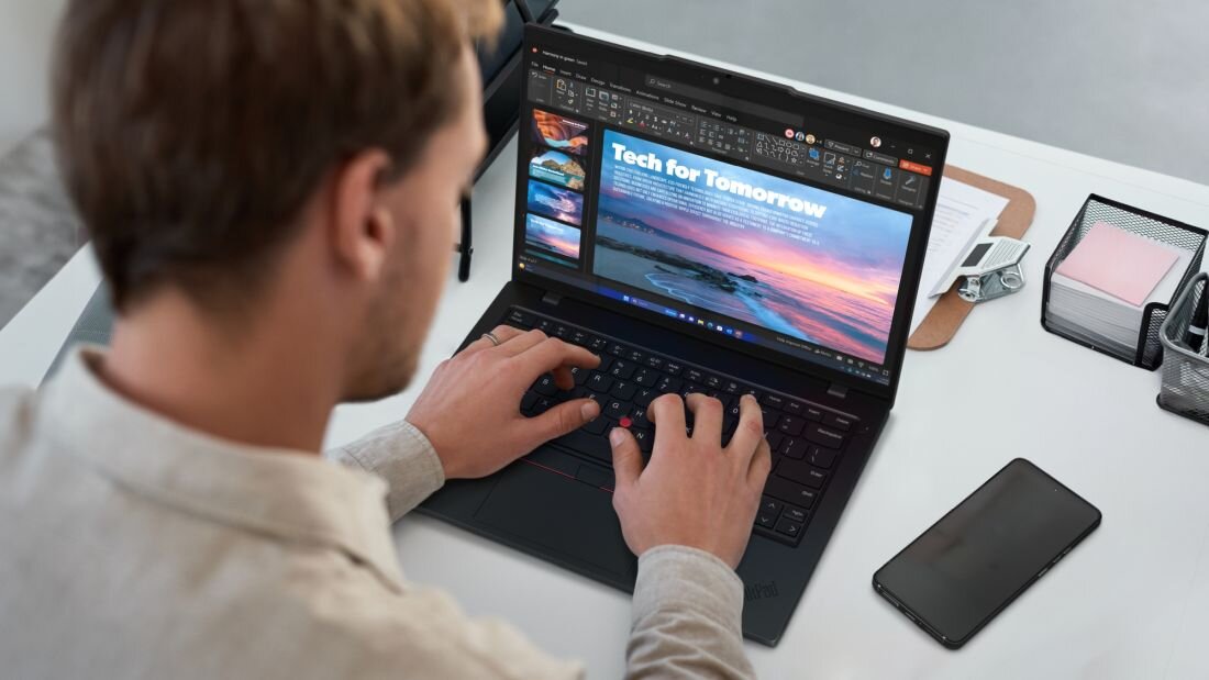 Mężczyzna w białym swetrze pracujący na laptopie Lenovo ThinkPad z prezentacją Tech for Tomorrow na ekranie. - RAM DDR5, dysk SSD