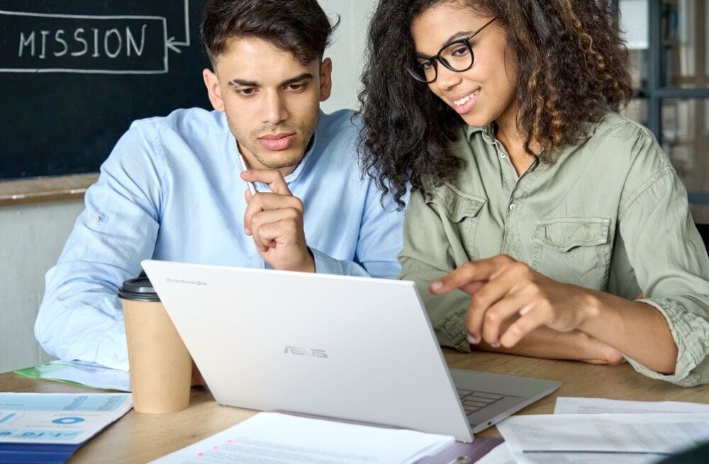 Laptop ASUS Chromebook Plus CB3402CVA Młody mężczyzna i młoda kobieta siedzą przy stole w pomieszczeniu biurowym, patrząc na ekran laptopa. Kobieta wskazuje coś na ekranie, podzespoły, procesor, rdzenie, taktowanie, pamięć RAM