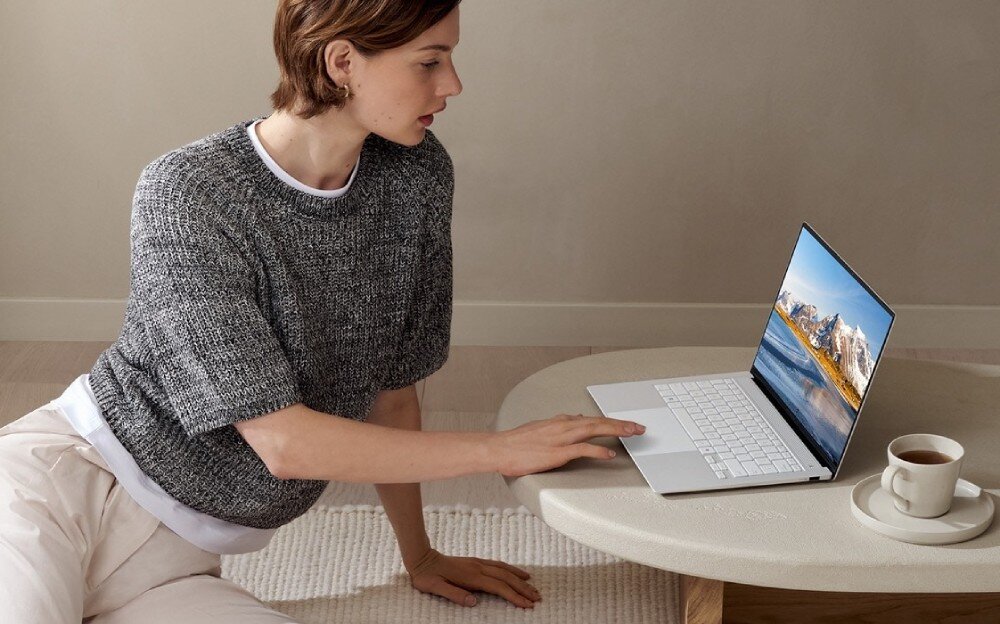 Laptop ASUS ZenBook S 14 UX5406SA-PV030W Kobieta siedząca przy niskim stoliku, dotyka touchpada otwartego laptopa stojącego na blacie, wyświetlacz, przekątna, obraz