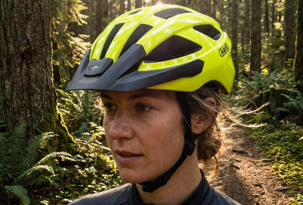 Kask rowerowy ABUS Macator Signal Żółty Szosowy rozmiar M, 58-62 cm osoba w kasku patrzy przed siebie w tle góry szlak bezpieczeństwo uniwersalna ochrona głowy
