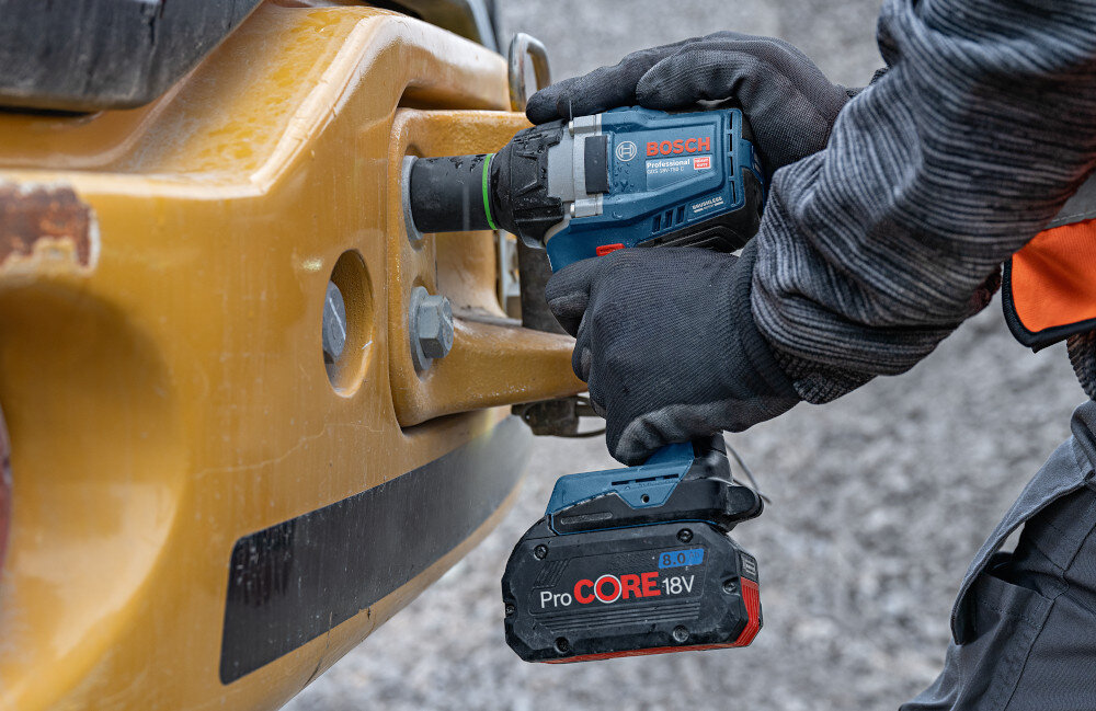 Klucz udarowy BOSCH GDS 18V-750 plac budowy osoba dokręca śruby w samochodzie za pomocą klucza do szybkiego i skutecznego dokręcania oraz odkręcania śrub i nakrętek wysoki moment obrotowy mechanizm udarowy bezproblemowe odkręcanie zapieczonych śrub