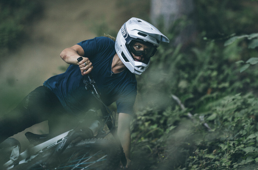 Kask rowerowy ABUS HiDrop Moss Zielony MTB (rozmiar M) osoba w kasku jedzie na rowerze rozmazane tło daszek ochrona przed promieniami słonecznymi zwisającymi gałęziami technologia Break-Away-Visow razie upadku daszek samoczynnie odłączył się od kasku