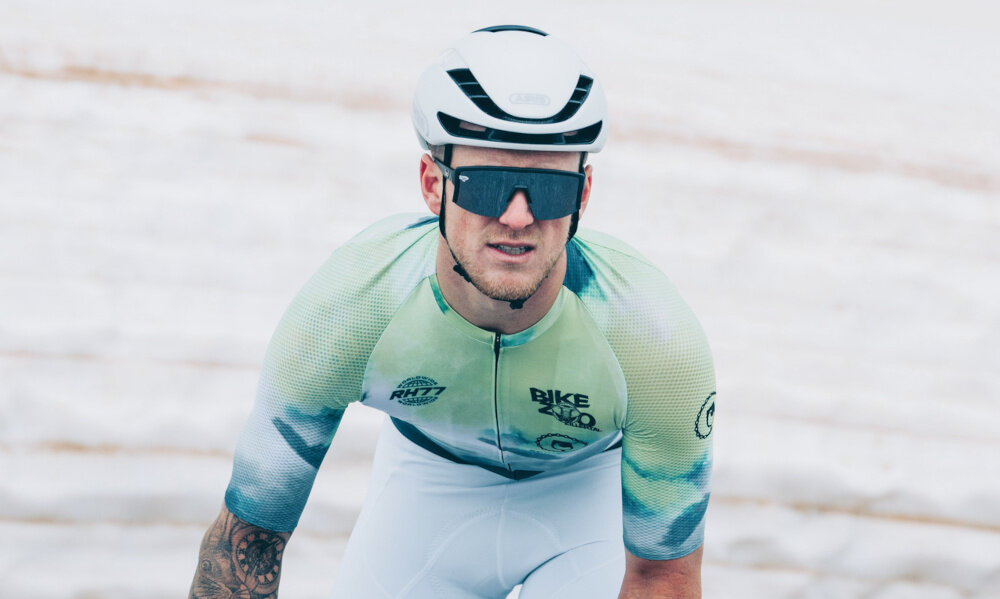 Kask rowerowy ABUS Gamechanger Polar Biało-czarny Szosowy rozmiar L, 59-62 cm osoba w kasku jedzie na rowrze po szosie w tle łąka pola bezpieczeństwo aerodynamiczna jazda