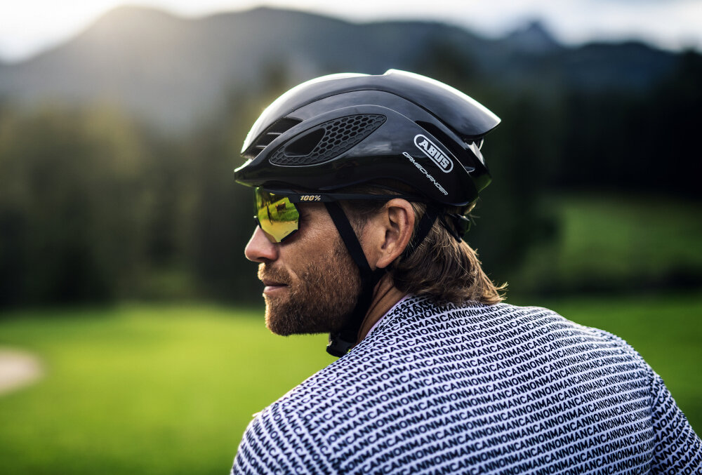 Kask rowerowy ABUS Gamechanger Velvet Czarny Szosowy rozmiar L, 59-62 cm krajobraz las łąka osoba w kasku widoczna z boku bezpieczeństwo aerodynamiczna jazda