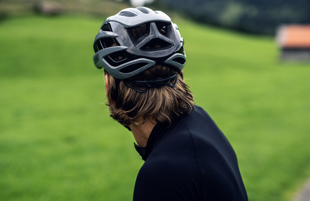 Kask rowerowy ABUS AirBreaker Czarny Szosowy rozmiar M osoba w kasku odwrócona tyłem w tle trawa wydajna ochrona wentylacja bezpieczna jazda na szosie