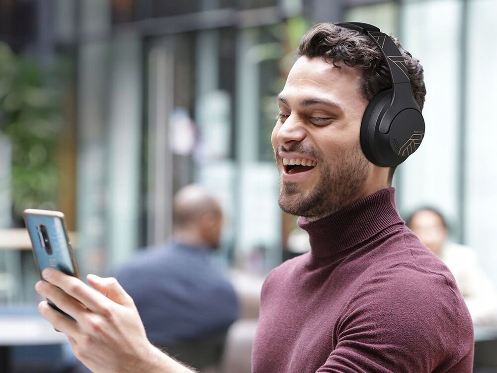 Słuchawki nauszne POWERLOCUS P3 tryb gamingowy niskie opóźnienia, osoba z załozonymi słuchawkami nausznymi z telefonem w ręku