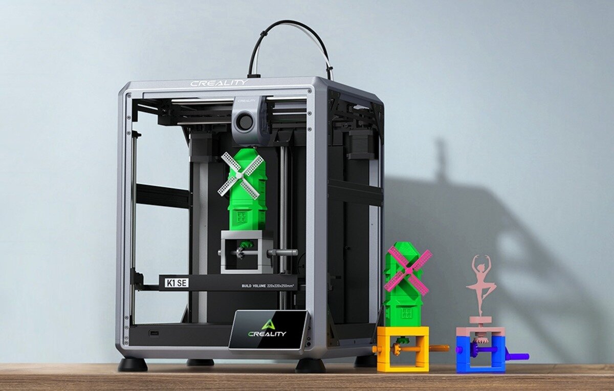 Drukarka 3D Creality K1 SE z zielonym wiatrakiem w środku i modelami obok na drewnianym blacie