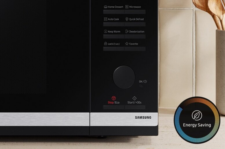 Czarna kuchenka mikrofalowa z panelem sterowania zawierającym przyciski takie jak Home Dessert, Auto Cook, Quick Defrost, Keep Warm, Deodorization, Lock(3 sec), Favorite oraz pokrętło OK/◦. Na dole widoczne są przyciski Stop/Eco i Start/+30s, a na srebrnym pasku logo SAMSUNG.