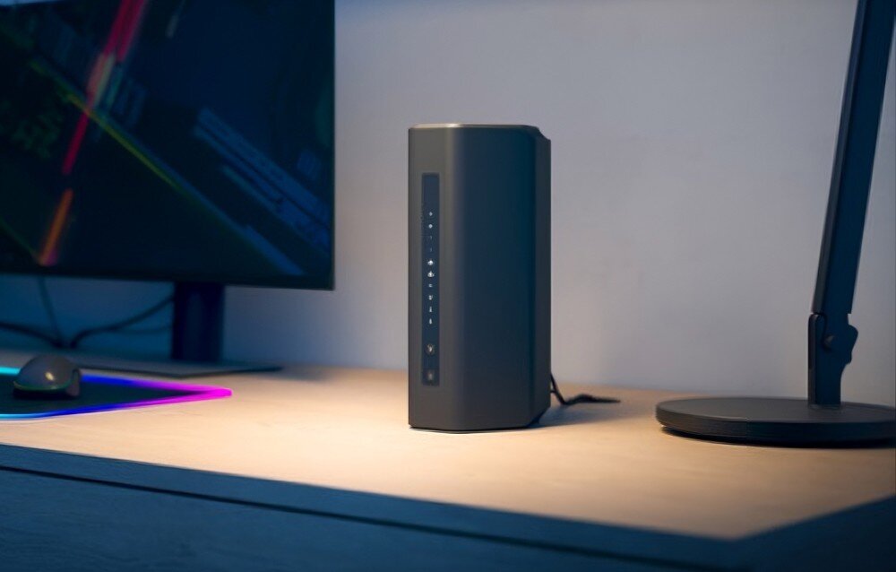 Router NETGEAR Nighthawk RS300 Pionowy router na biurku z panelem diod z przodu w tle monitor komputerowy i lampa biurkowa, opis