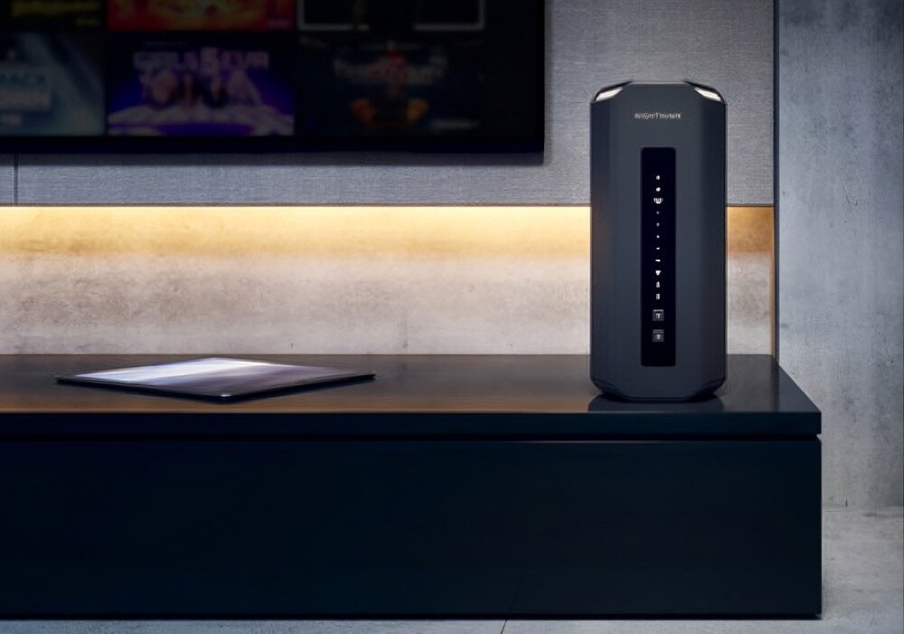 Router NETGEAR Nighthawk RS300 Pionowy router stojący na szafce w salonie podświetlanej od spodu diodami LED w tle ekran telewizora z interfejsem serwisu streamingowego, zabezpieczenia, firewall