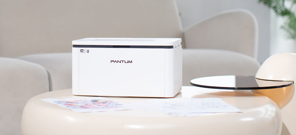 Drukarka PANTUM BP2300W Wi-Fi, Bluetooth prezentacja drukarki w jasnym pokoju na stoliku obok kartki nadrukowane za stolikiem jasna kanapa