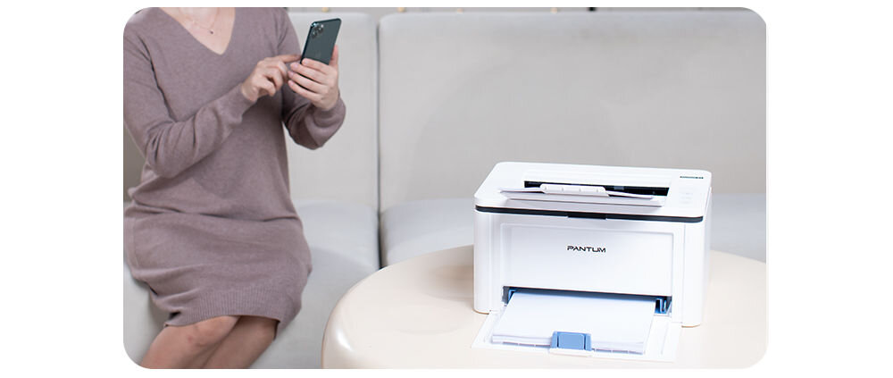 Drukarka PANTUM BP2300W Wi-Fi, Bluetooth prezentacja drukarki stojącej na jasnym stoliku obok kobieta siedząca z telefonem w dłoni na jasnej kanapie drukowanie bezprzewodowe Wi-Fi Bluetooth AirPrint Mopria szybka i prosta konfiguracja urządzenia