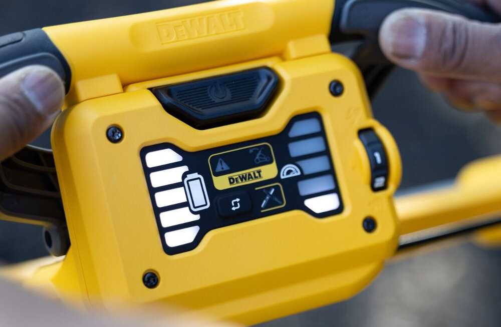 Kosiarka akumulatorowa DEWALT DCMWSP550N-XJ z napędem zbliżenie na panel osoba trzyma dłonie na kierownicy czytelny panel LED informacje o stanie naładowania akumulatora zużyciu noża ewentualnych problemach z układem tnącym wskaźnik obciążenia sygnalizuje moment zwiększonego poboru mocy pomaga dostosować tempo pracy stały podgląd parametrów