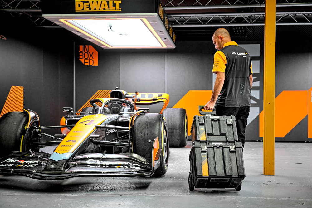 Zestaw skrzyni na narzędzia DEWALT McLaren 3 w 1 DWST60452-1 pomieszczenie osoba ciągnie za sobą skrzynie w tle samochód McLaren trzy skrzynie mobilny dobrze zorganizowany system przechowywania pomaga uporządkować narzędzia akcesoria i sprzęt elektroniczny duża efektywność pracy