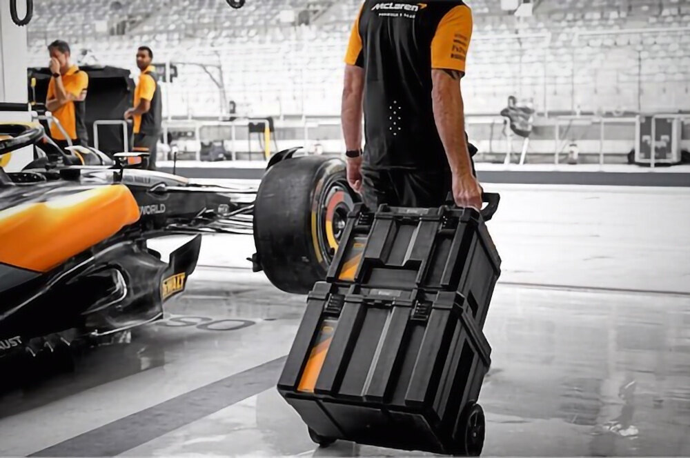 Zestaw skrzyni na narzędzia DEWALT McLaren 3 w 1 DWST60452-1 garaż samochodowy osoba ciągnie za sobą skrzynie w tle samochód McLaren teleskopowy uchwyt koła o średnicy 7 cali przycisk blokujący uchwyt oszczędność czasu