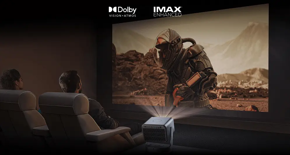 Projektor wyświetla na dużym ekranie film z astronautą. Widoczne porty urządzenia i osoby na fotelach kinowych. Widoczne ikony oznaczenie jakości Imax Enhanced i logo technologii Dolby Vision, Dolby Atmos.