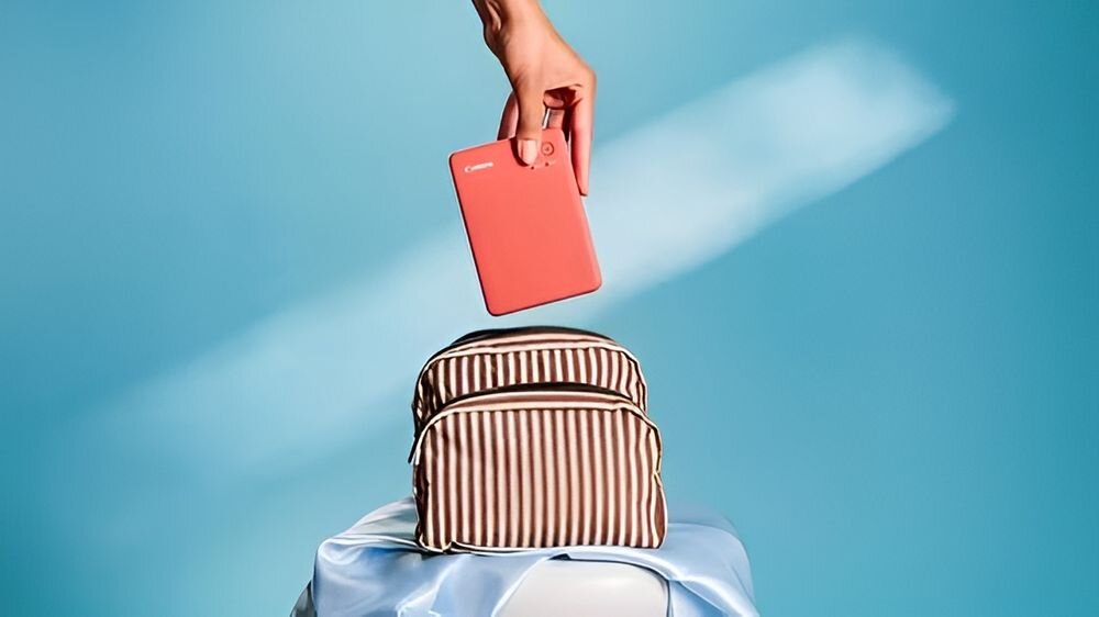 Drukarka CANON Selphy Square QX20 Druk w kolorze, Wi-Fi Biały pokazanie wkładania urządzenia do małego plecaka niebieskie tło wymiary mieści się w małej torebce waga utrwalanie wyjątkowych chwil