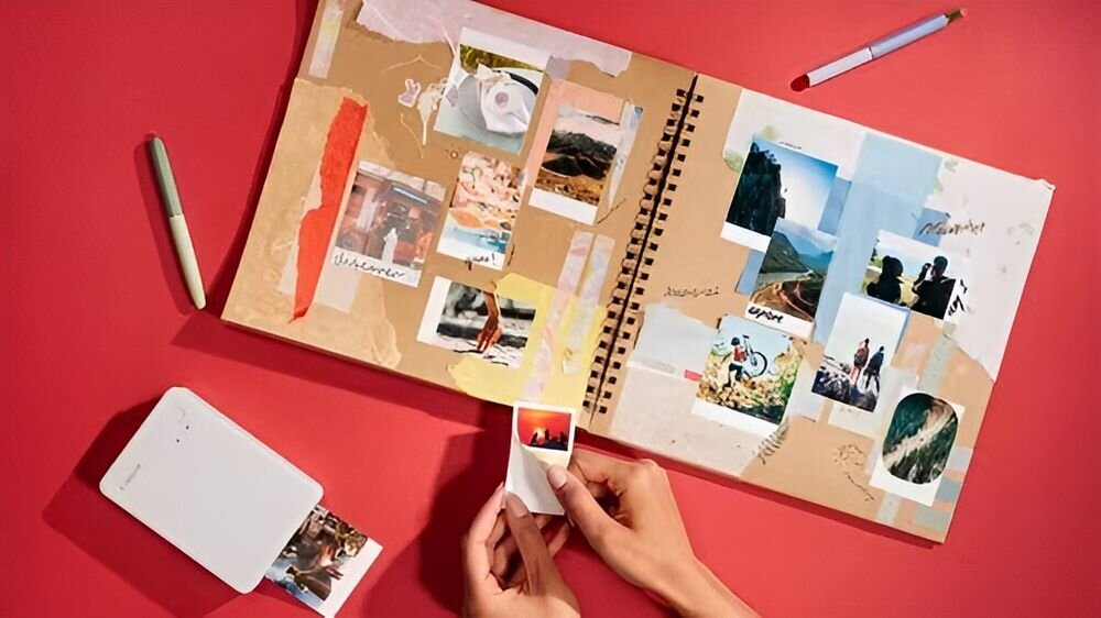 Drukarka CANON Selphy Square QX20 Druk w kolorze, Wi-Fi Biały drukarka na czerwonym tle podczas drukowania obok album ze zdjęciami samoprzylepny papier naklejka personalizacja przedmiotów