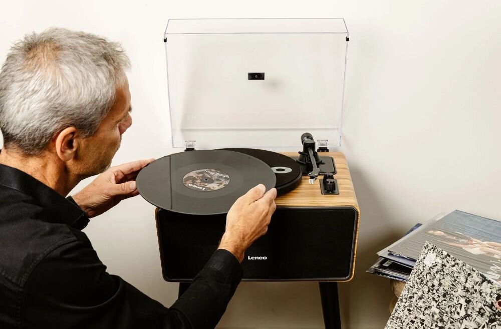 Gramofon LENCO LS-570OK Bluetooth 5.0 napęd paskowy cztery głośniki obudowa w kolorze drewna, osoba umieszczająca płytę do gramofonu