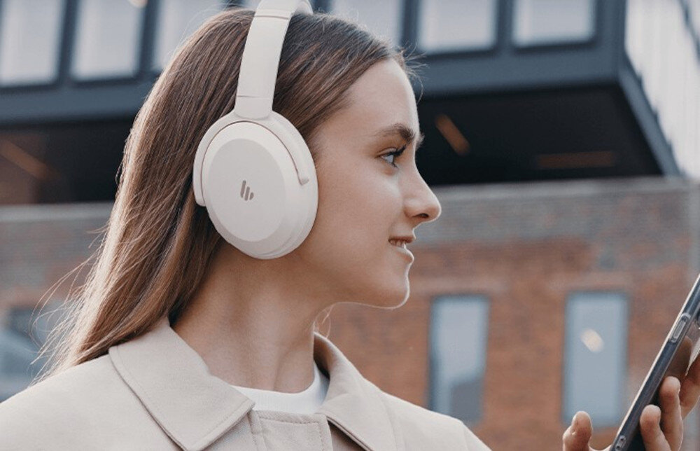 Słuchawki nauszne EDIFIER WH700NB Pro ANC z szerokim pasmem dźwięku i komfortową konstrukcją, osoba z założonymi słuchawkami nausznymi z telefonem w ręku