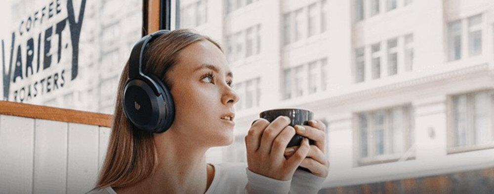 Słuchawki EDIFIER WH700NB Pro ANC z mikrofonem AI do czystych rozmów głosowych, osoba z założonymi słuychawkami nausznymi z kubkiem w rękach