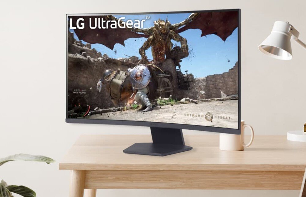 Monitor LG UltraGear 32GS60QC-B.AEUQ Monitor ustawiony na drewnianym biurku, wyświetlający grę z postacią w zbroi walczącą z dużym smokiem. Obok monitora stoi biała lampka biurkowa i biały kubek, opis
