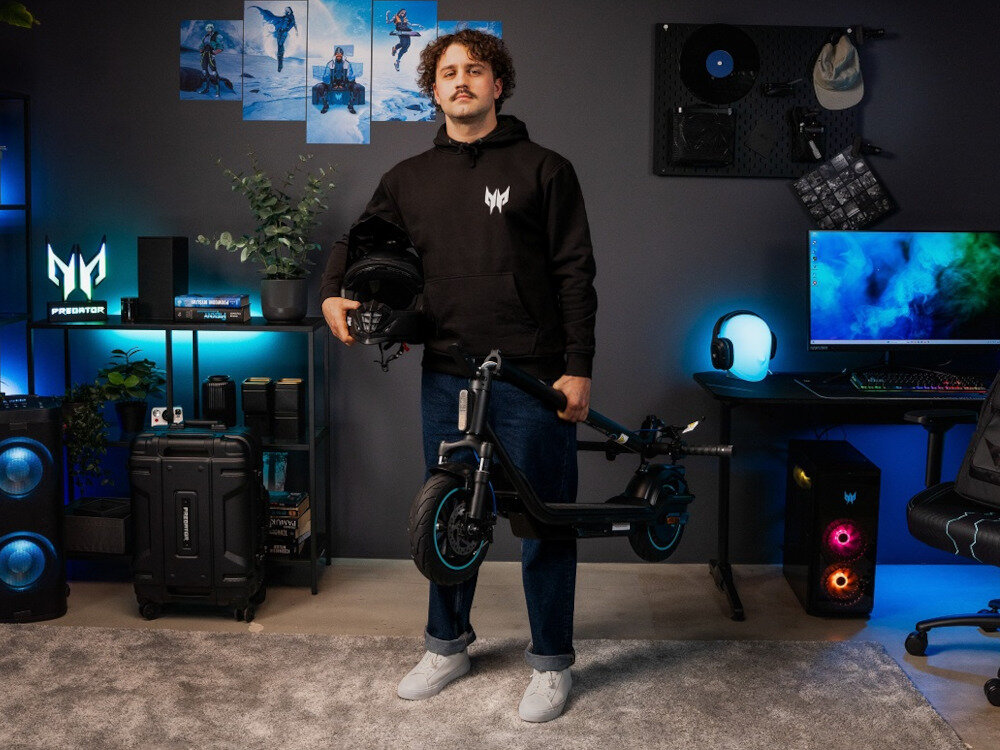 Hulajnoga elektryczna ACER PREDATOR Series ES Storm 60km 500W Amortyzacja 10 cali Czarny mężczyzna stoi w pokoju trzymając w ręce złożoną hulajnogę solidna konstrukcja niewielkie wymiary składany mechanizm łatwe przenoszenie i przechowywanie