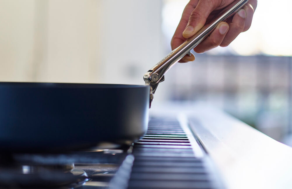 JJ--Patelnia 20cm ze składanym uchwytem Space ręka trzymająca srebrny uchwyt niebieska powłoka patelnia na płycie grzewczej jasne tło trwałość zdrowe gotowanie korpus wykonany z solidnego aluminium równomierne rozprowadzanie ciepła wewnętrzna powłoka ceramiczna nie przywiera smażenie bez użycia tłuszczu bezpieczeństwo użytkowania brak szkodliwych substancji PTFE, PFAS, PFOA, ołów kadm standardowa średnica patelni różnorodne, tradycyjne potrawy jakość, zdrowie i wygoda