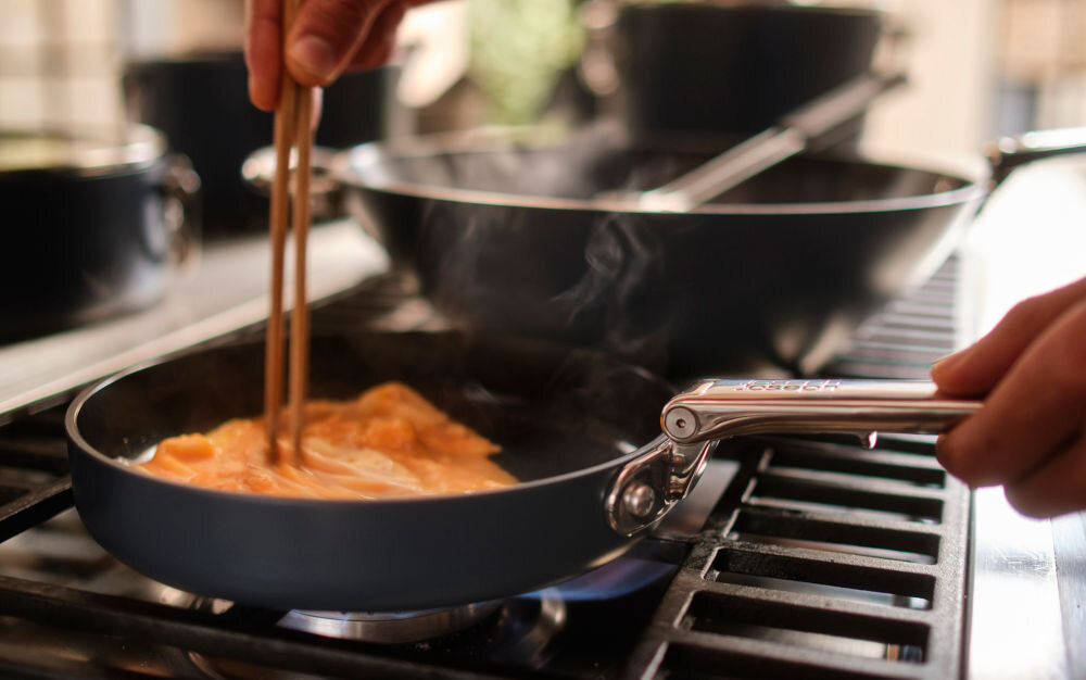 JJ--Patelnia 20cm ze składanym uchwytem Space osoba pałeczkami miesza danie na patelni srebrna rączka niebieska powłoka kuchenne tło na różnych typach kuchenek: gazowych, elektrycznych, ceramicznych indukcyjnych do współczesnych kuchni wysoka jakość materiałów trwałość można jej używać w piekarniku do temperatury maksymalnej 232°C funkcjonalność