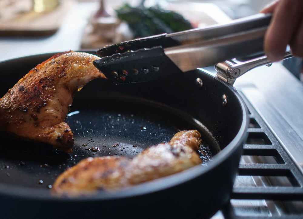 JJ-Patelnia 28cm ze składanym uchwytem Space patelnia na palniku osoba obraca szczypcami mięso znajdujące się na patelni 