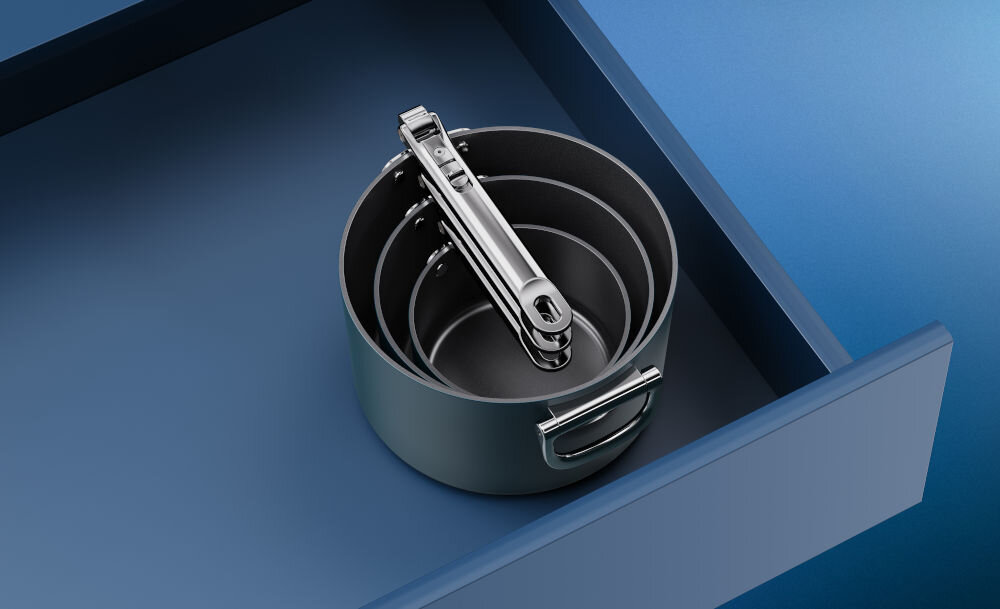 JJ-Zestaw rondli ze skł.uchwytami +pokrywk++ Space różne wielkości czarne dno srebrne uchwyty rondle stoją w niebieskiej szufladzie białe tło nadają się do mycia w zmywarce zachowanie właściwości powłoki nieprzywierającej zalecane jest mycie ręczne uniknięcie ewentualnego uszkodzenia przedłużenie żywotności naczyń