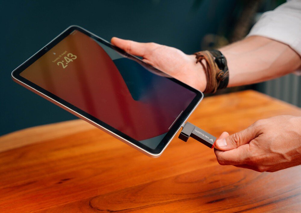 Pendrive VERBATIM Dual QuickStick Dłoń trzymająca szary pendrive z napisem 'verbatim' na tle monitora wyświetlającego okno z postępem przesyłania danych