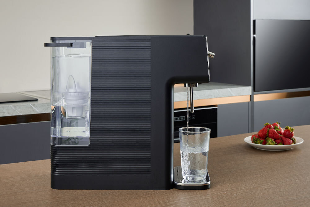 Dyspenser do wody PHILIPS ADD5962BK/10 Profil czarnego dystrybutora wody Philips nalewającego przefiltrowaną wodę do szklanki; widoczny przezroczysty zbiornik z filtrem z tyłu urządzenia.
