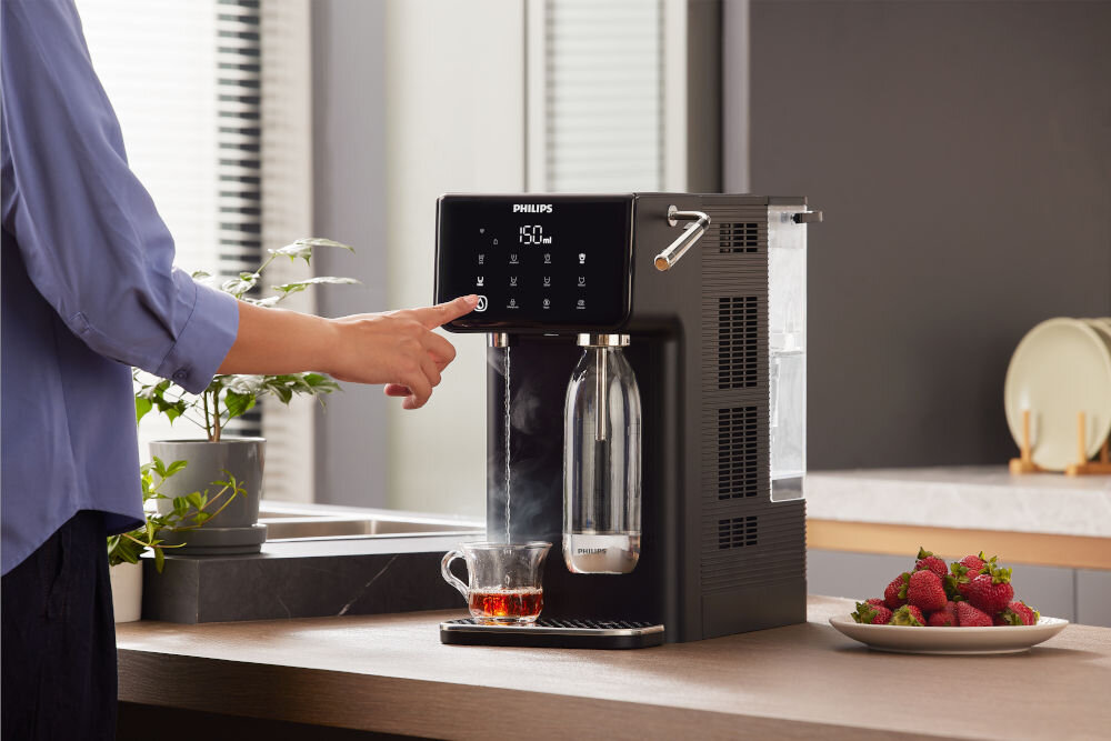 Dyspenser do wody PHILIPS ADD5962BK/10 Dystrybutor wody Philips nalewający gorącą wodę do filiżanki z herbatą; widoczna unosząca się para wodna.