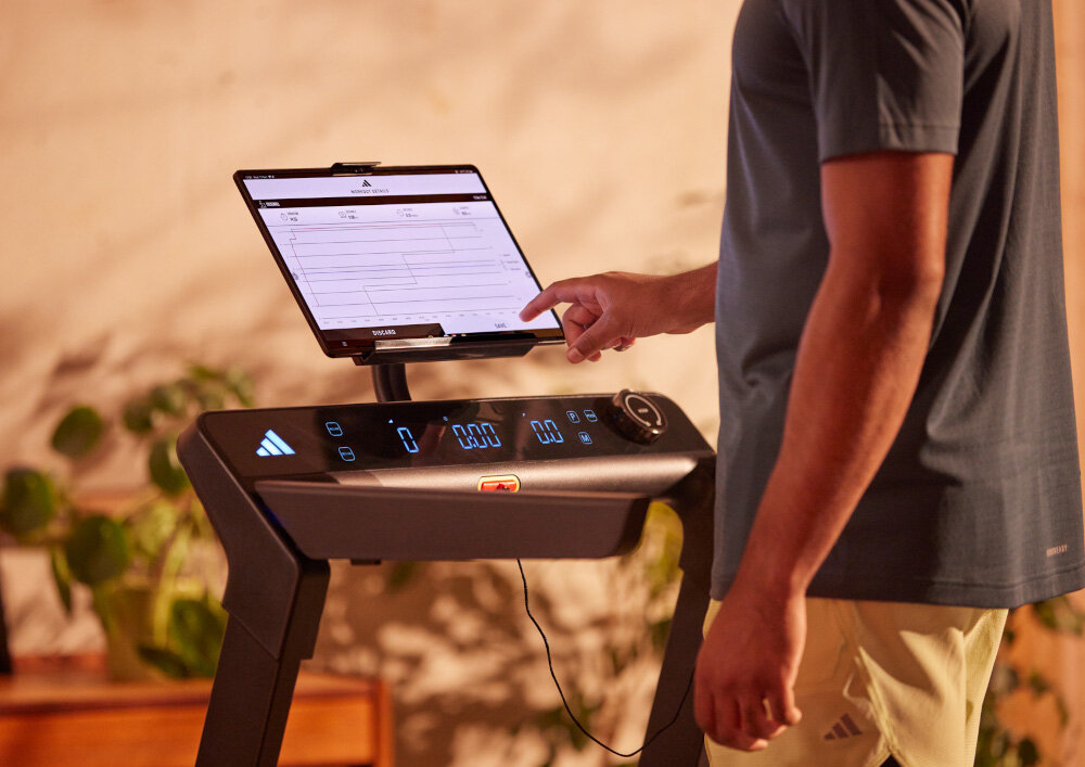 Bieżnia elektryczna ADIDAS T-24C 1470W 18km-h pokój zbliżenie na uchwyt na tablet na uchwycie tablet osoba dotyka ekranu tabletu ADIDAS Console+ Bluetooth dostęp do treningów statystyk i indywidualnej analizy postępów kompatybilność z aplikacją Zwift integracja z aplikacją Kinomap