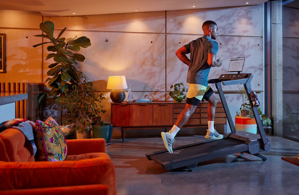 Bieżnia elektryczna ADIDAS T-24C 1470W 18km-h pokój bieżnia ustawiona na podłodze na bieżni biegnie osoba w tle komoda kwiaty meble kółka transportowe wygodne przesuwanie sprzętu regulacja poziomu podłogi można wypoziomować bieżnię trening jest stabilny i bezpieczny maksymalne obciążenie do 110 kg solidność konstrukcji