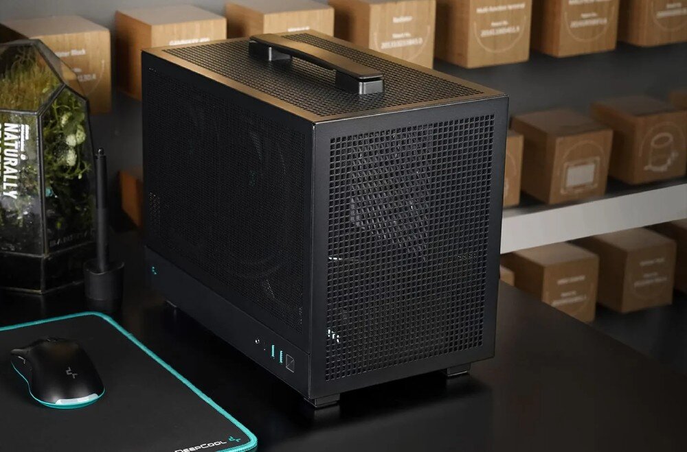 Obudowa DEEPCOOL CH160 Mesh Komputer w czarnej obudowie stojący na biurku, wyposażony w rączkę do przenoszenia na górnym panelu, z widocznym w tle monitorem i klawiaturą