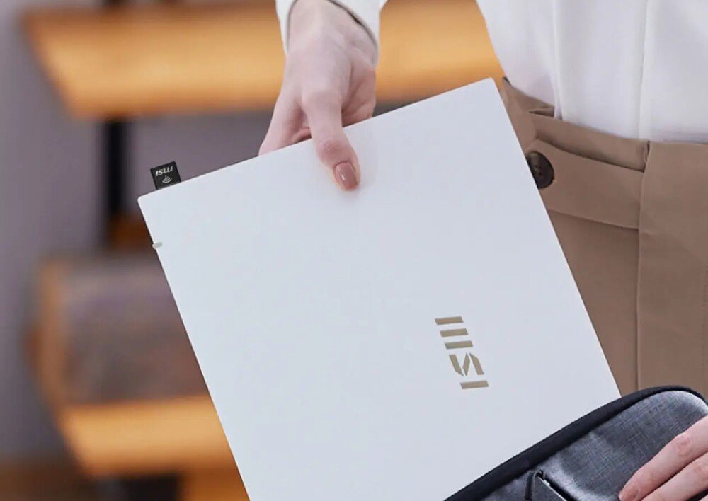 Karta sieciowa MSI AX1800 Nano GUAX18N Zbliżenie na dłonie trzymające biały laptop z wpiętym w boczny port USB miniaturowym adapterem podczas wkładania komputera do szarej torby