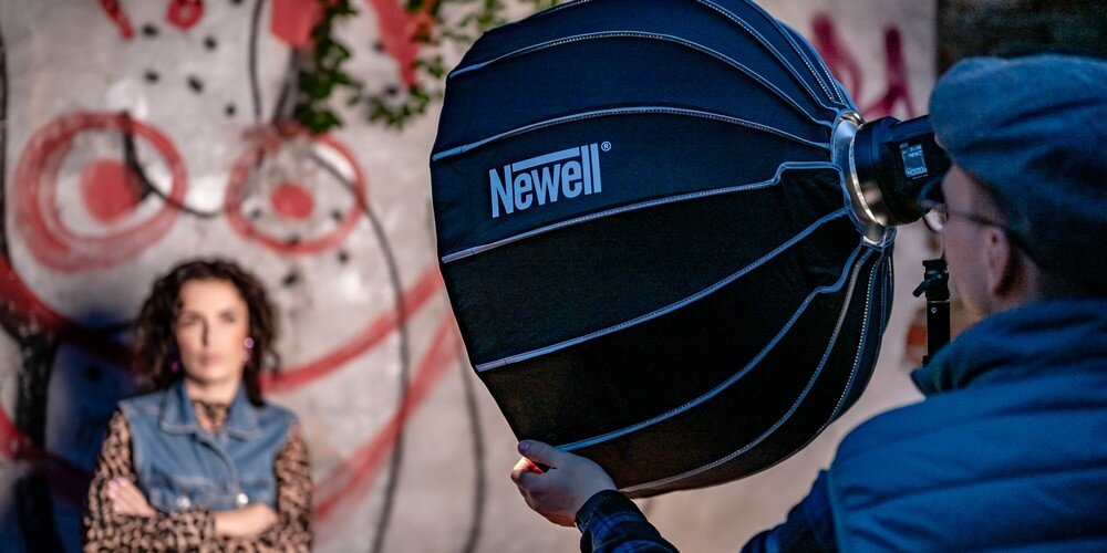 Softbox paraboliczny Newell 65 cm rozłożony w trakcie sesji; fotograf ustawia softbox; w tle widoczna modelka