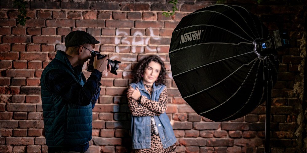 Softbox paraboliczny Newell 85 cm w trakcie sesji; fotograf patrzy przez wizjer aparatu; w tle modelka